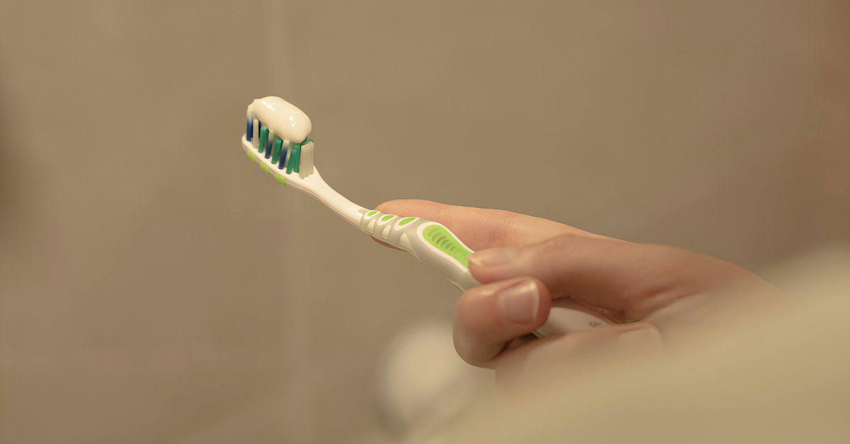 A person holds a green and white toothbrush after applying white toothpaste to the bristles