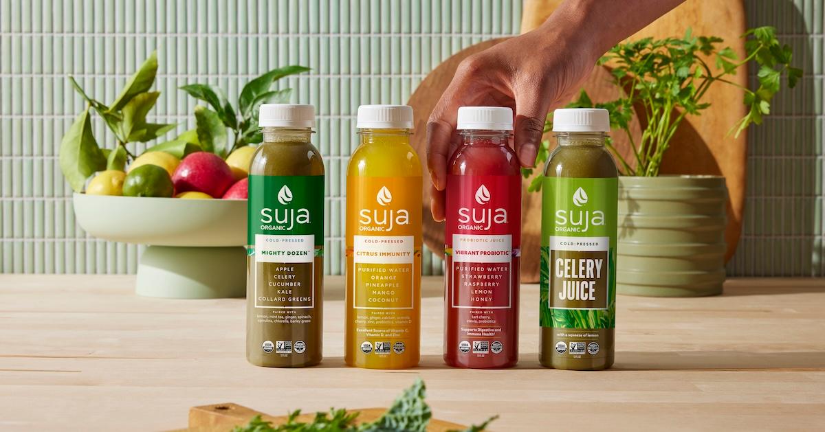 A hand reaches for one of four Suja Organic drink bottles on a countertop